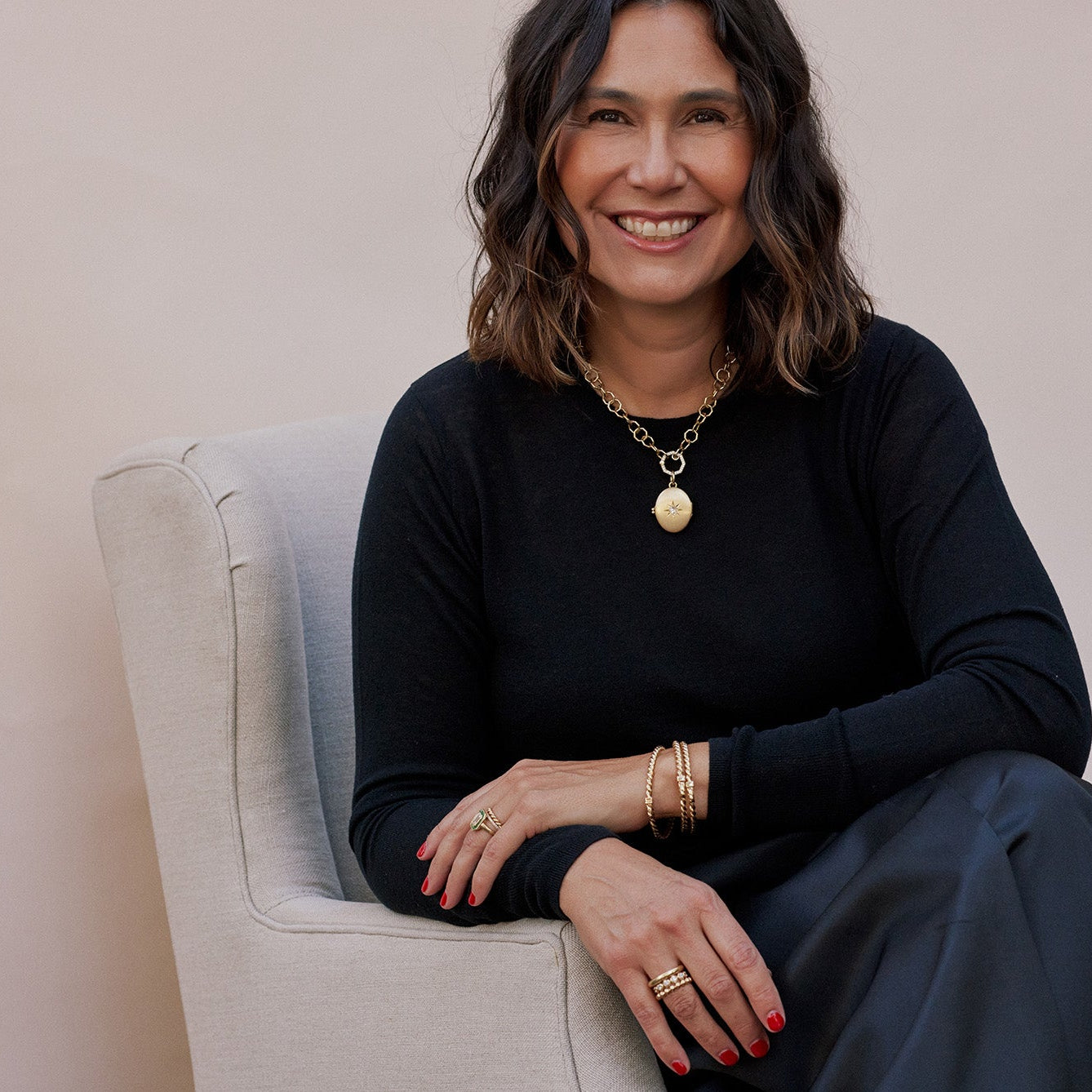 Designer Corina Madilian sitting in chair and smiling at the camera while wearing Single Stone jewelry