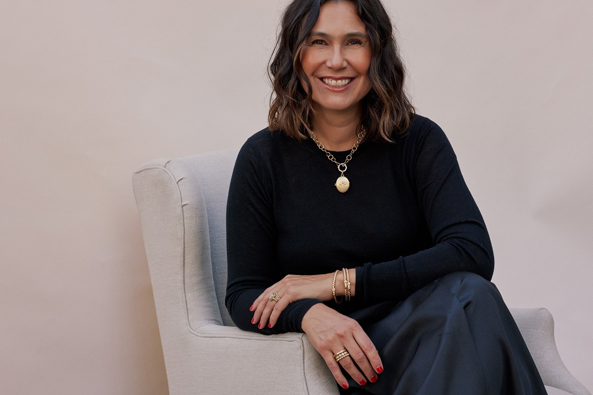 Designer Corina Madilian sitting in chair and smiling at the camera while wearing Single Stone jewelry