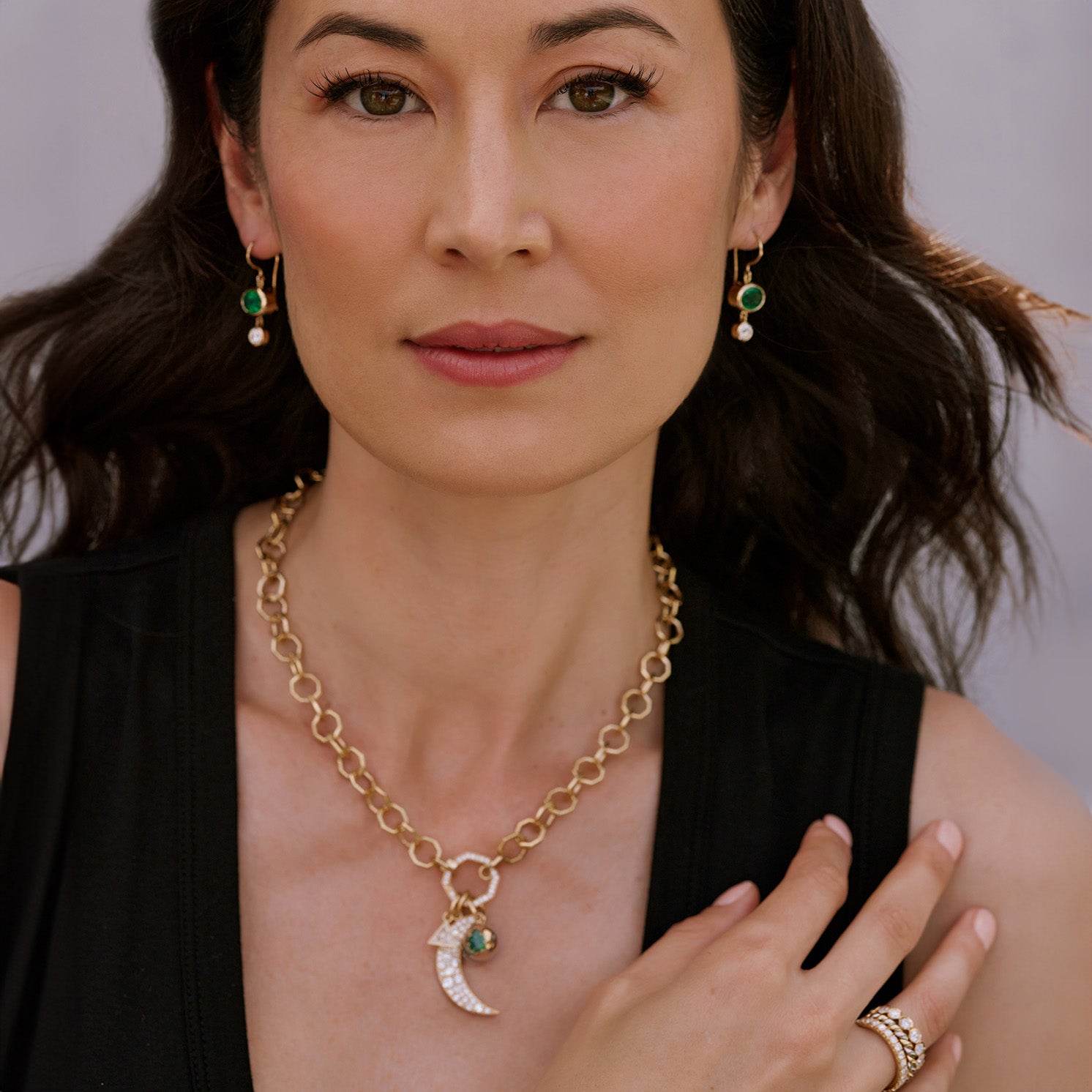 Woman looking at the camera wearing earrings, necklace with charms, and eternity bands from the Single Stone collection