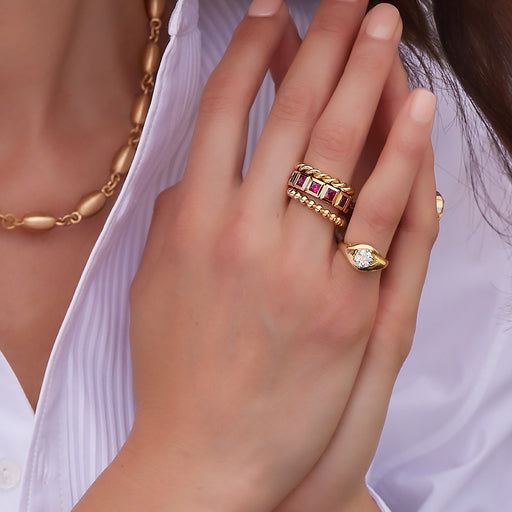 Woman's hand wearing several gold and ruby bands stacked on one finger and a diamond ring on the next finger, all from the Single Stone collection