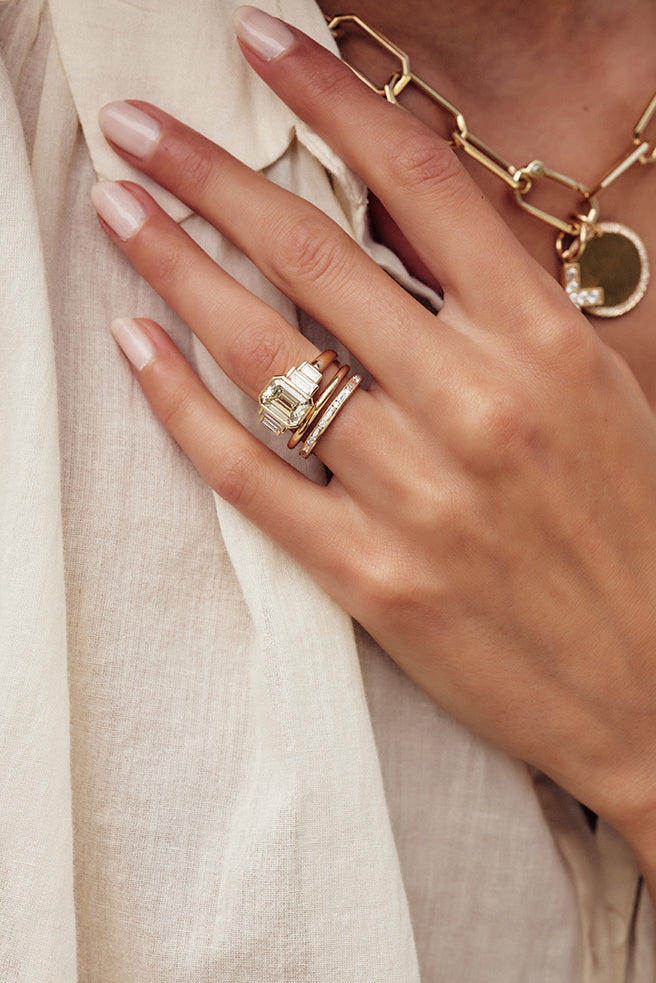 Woman's hand wearing Single Stone's Caroline ring featuring emerald cut diamond center with solid gold band and diamond eternity band below it