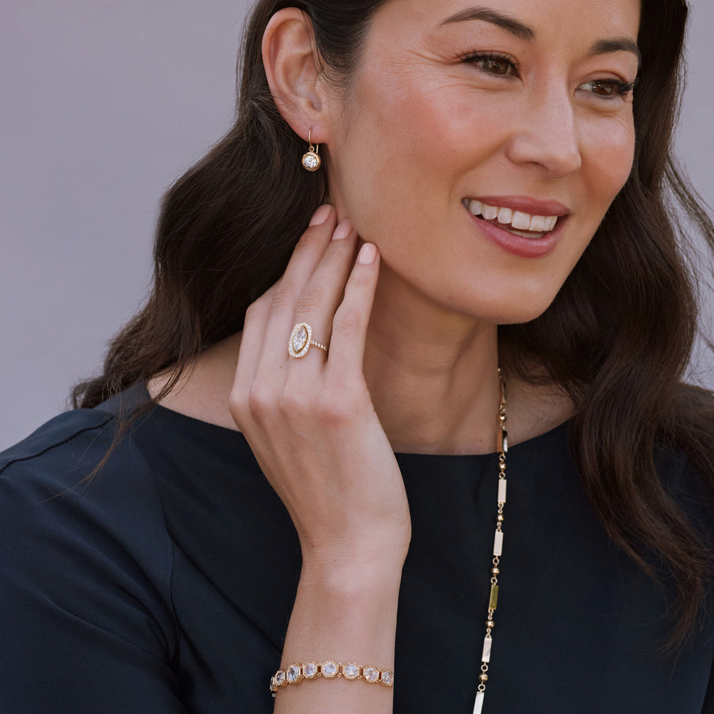 Woman wearing earrings, ring, necklace, and bracelet from the Single Stone collection, looking slightly off camera and smiling