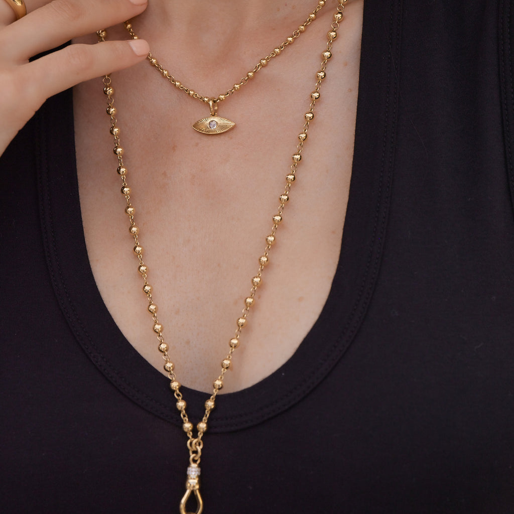 Two gold necklace chains with a diamond pendant hanging from the shorter one, all from the Single Stone collection, around a woman's neck with her hand touching one chain