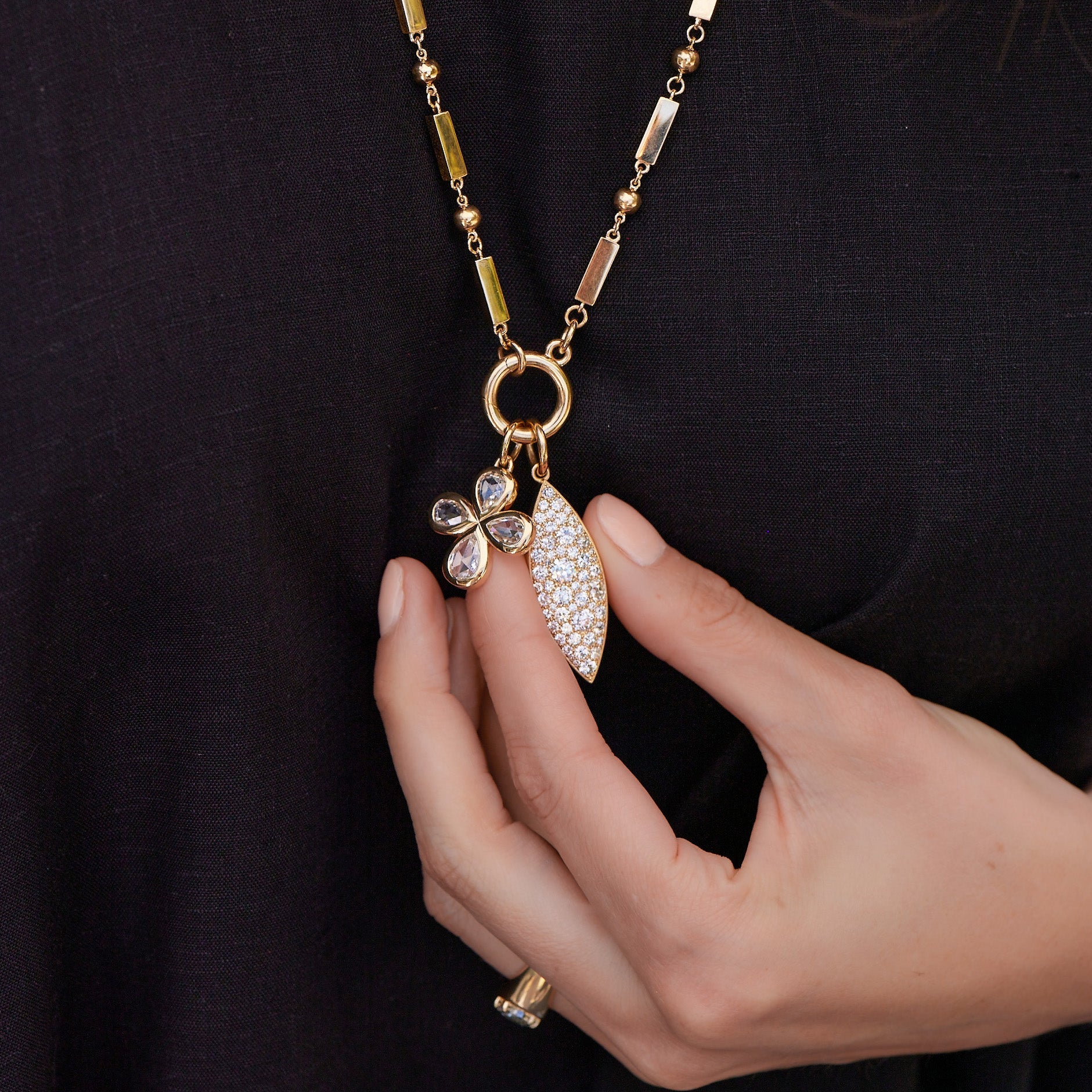 Woman's hand holding a diamond-covered charm hanging from a necklace chain next to a gold and diamond clover-shaped charm, all from the Single Stone collection