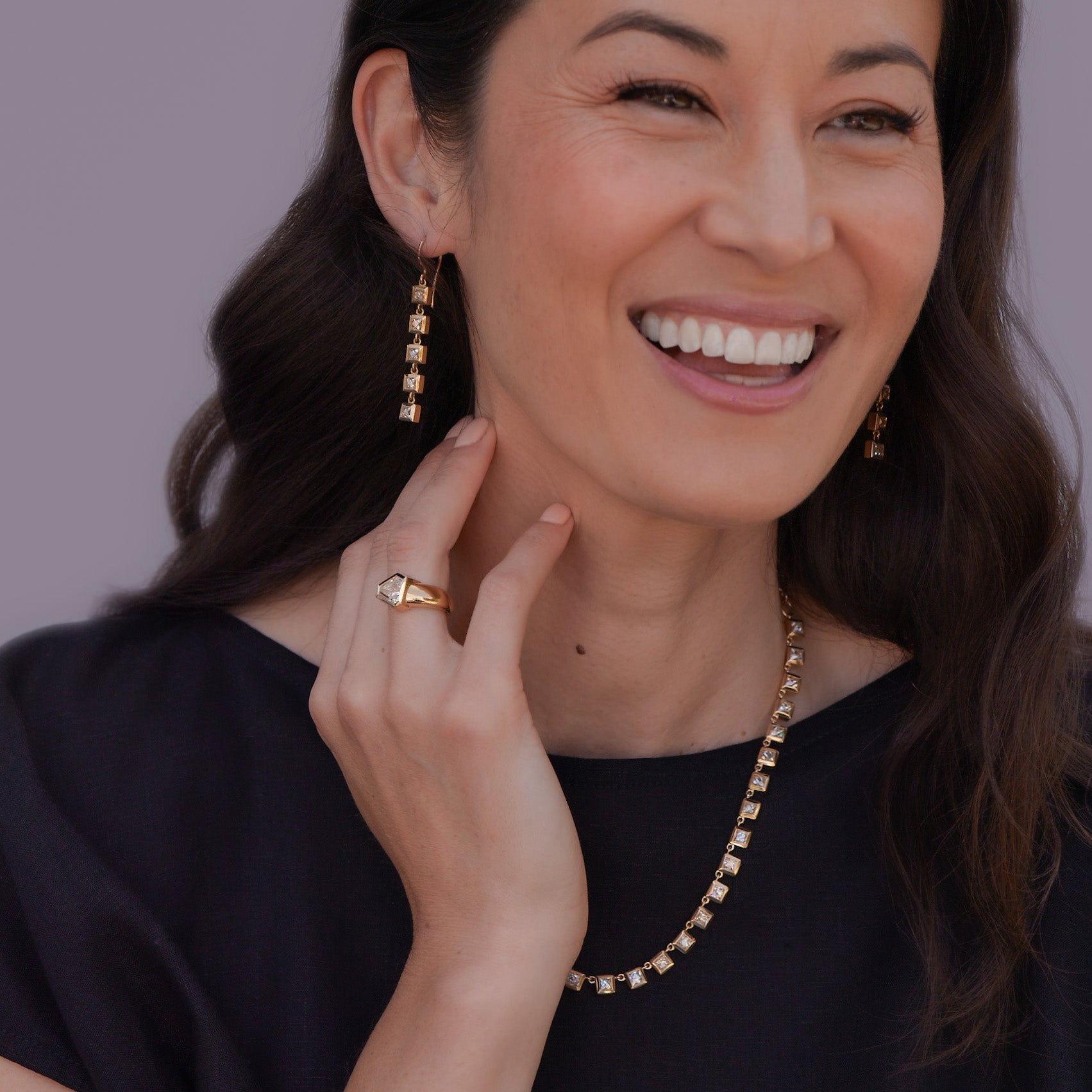 Woman wearing earring, ring, and necklace from Single Stone's Art Deco-inspired collection, looking slightly off camera and laughing