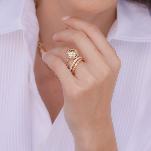 Close up of a woman's hands wearing several gold rings and bands from the Single Stone collection. She is holding her hands up close to her mouth and the Tahitian pearl necklace she's wearing is visible in the background.