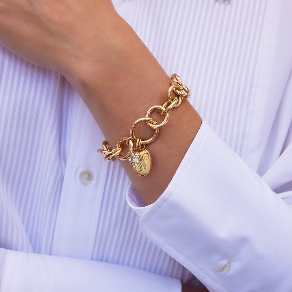 Woman's arm wearing a gold link bracelet with a monogrammed disc charm and a diamond pendant attached, all from the Single Stone collection