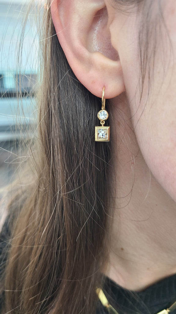 A French cut diamond and an old European cut diamond bezzle set in Single Stone's 'Karina' diamond double drop earring which hangs from a woman's ear