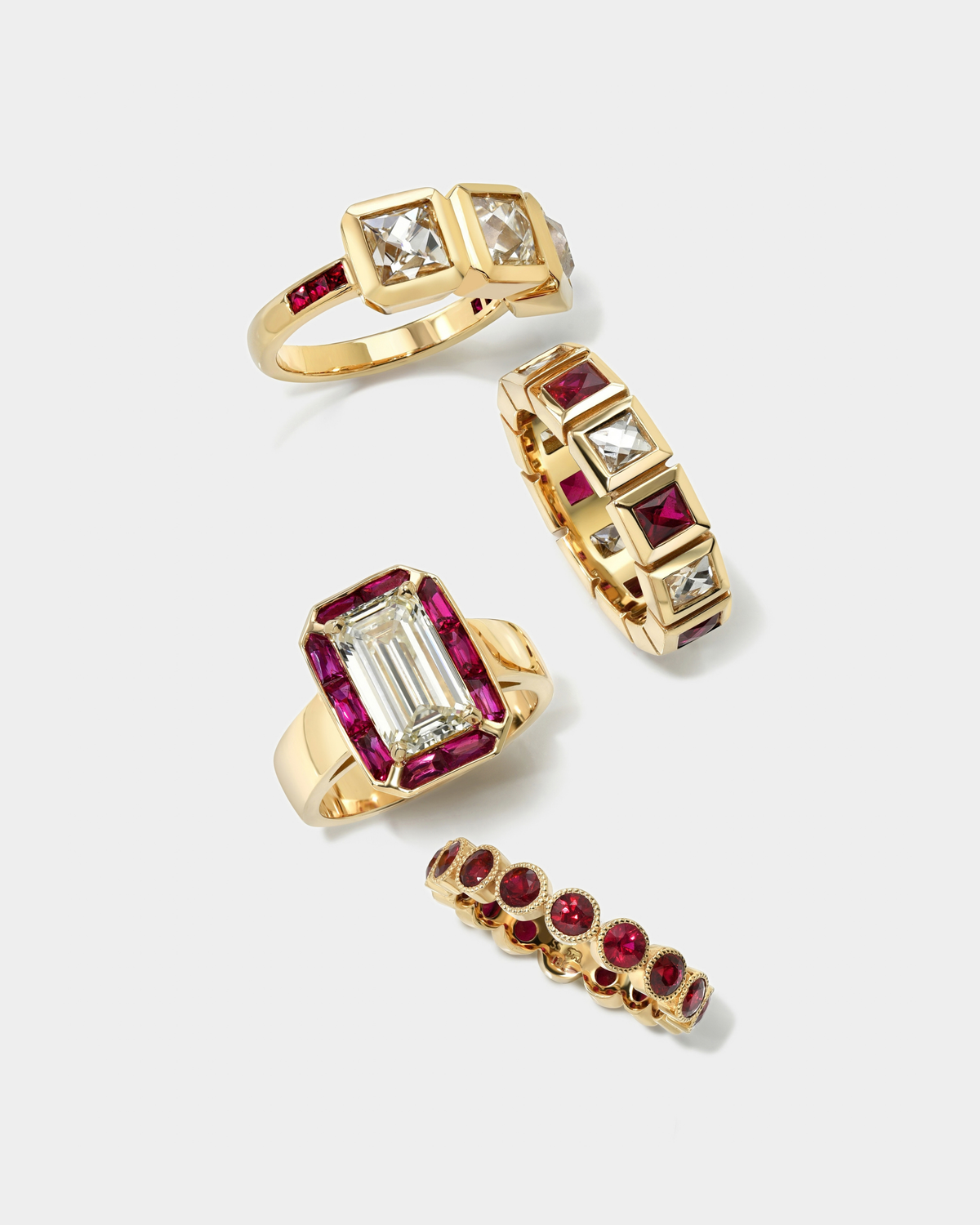 Four gold rings with red and clear gemstones, arranged on a light gray background.