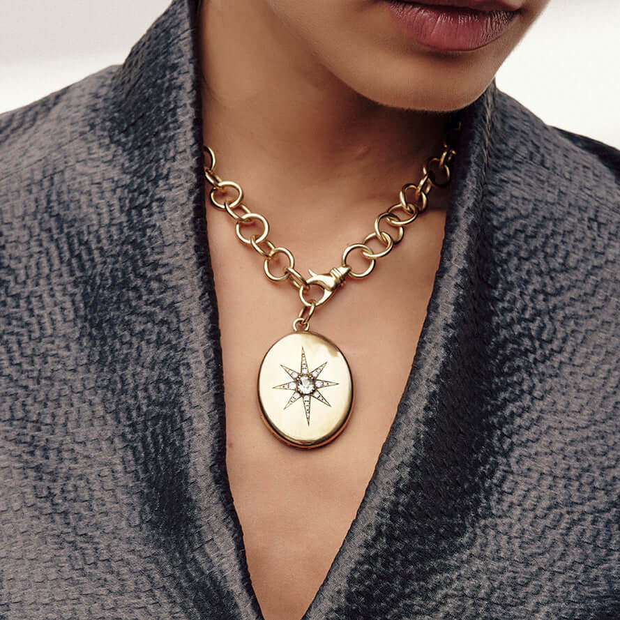 Woman wearing an oval-shaped pendant with a starburst design featuring an antique cushion cut diamond on a gold necklace chain