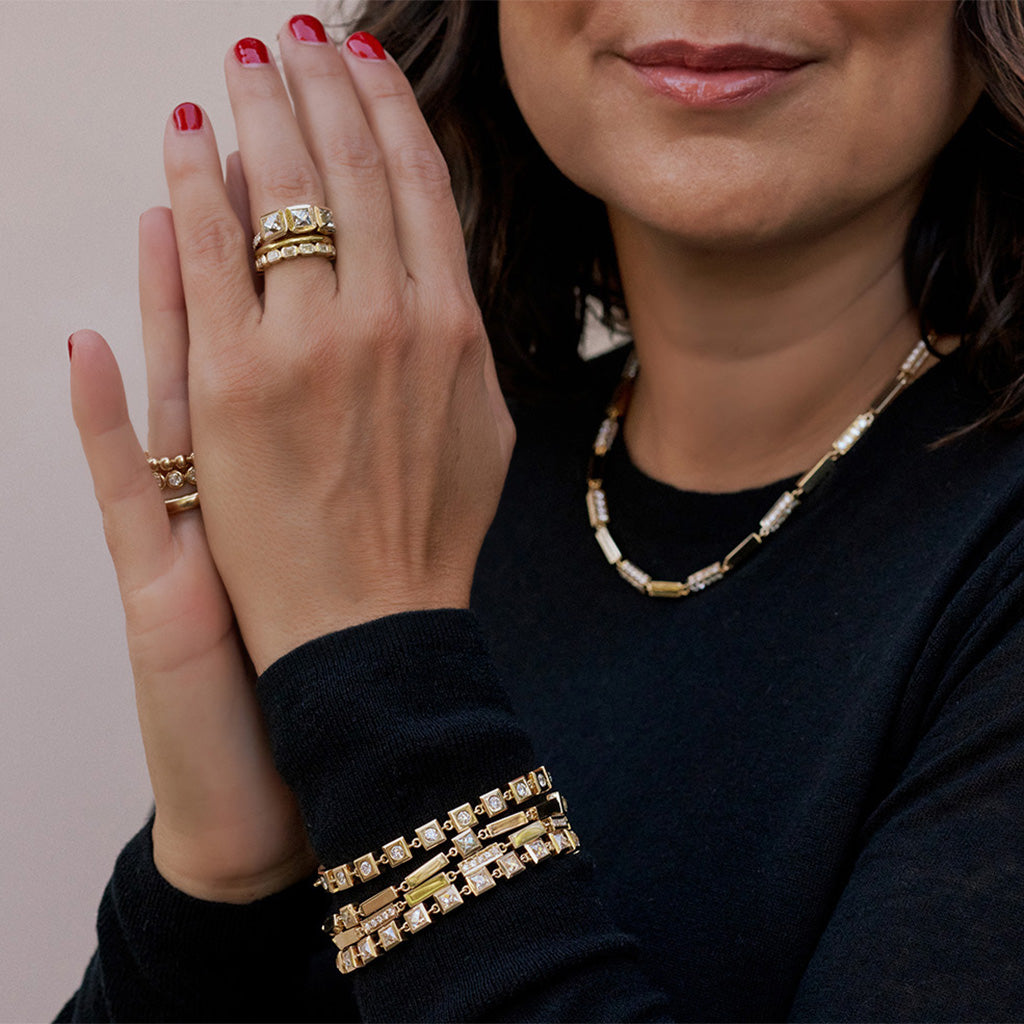 Close up of a woman wearing several gold bracelets, rings and bands from the Single Stone collection.