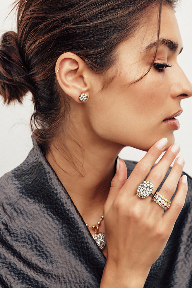 Profile shot of a woman wearing a large oval ring, small square-shaped stud earring, and a necklace with a heart-shaped pendant all from the Single Stone cobblestone collection. gold rings and bands from the Single Stone collection. She is also wearing a 