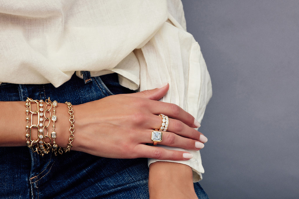 Woman's hand wearing Single Stone engagement ring and diamond eternity bands with several bracelets layered on her wrist