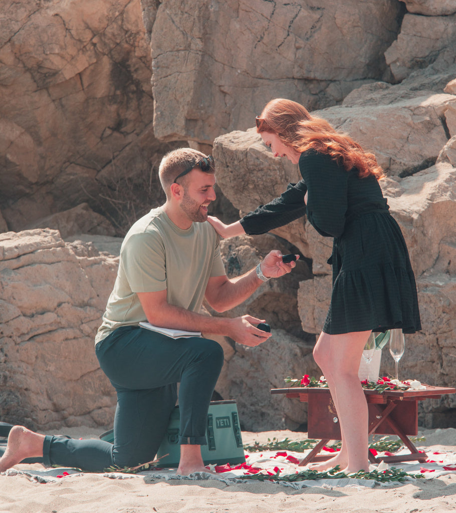 Tommy kneels on the beach with a ring box outstretched as he proposes to Kate, who is standing in front of him and looks happily surprised