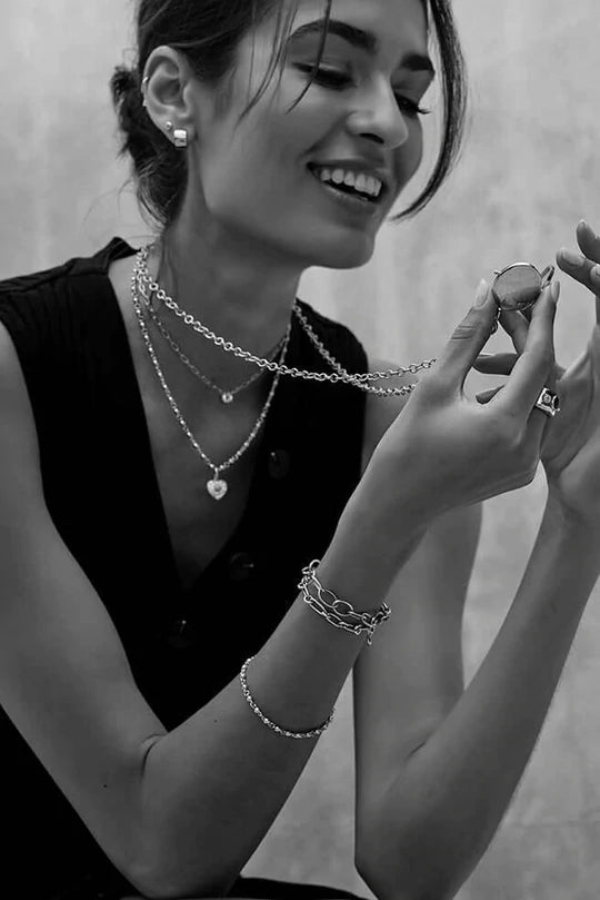 Model holding up an engravable vintage-style locket in yellow gold, with its chain around her neck, and smiling. Other Single Stone vintage-inspired necklaces are layered around her neck.
