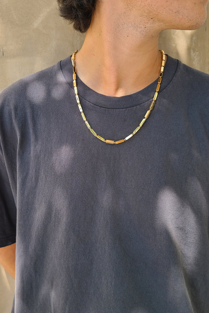 man in a gray shirt wearing a gold bar necklace