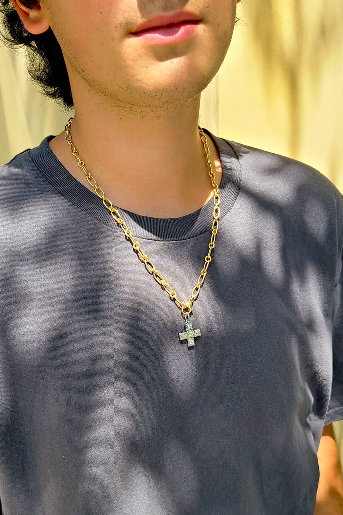 man in a gray shirt wearing a gold chain link necklace with a cross-shaped pendant featuring French cut diamonds