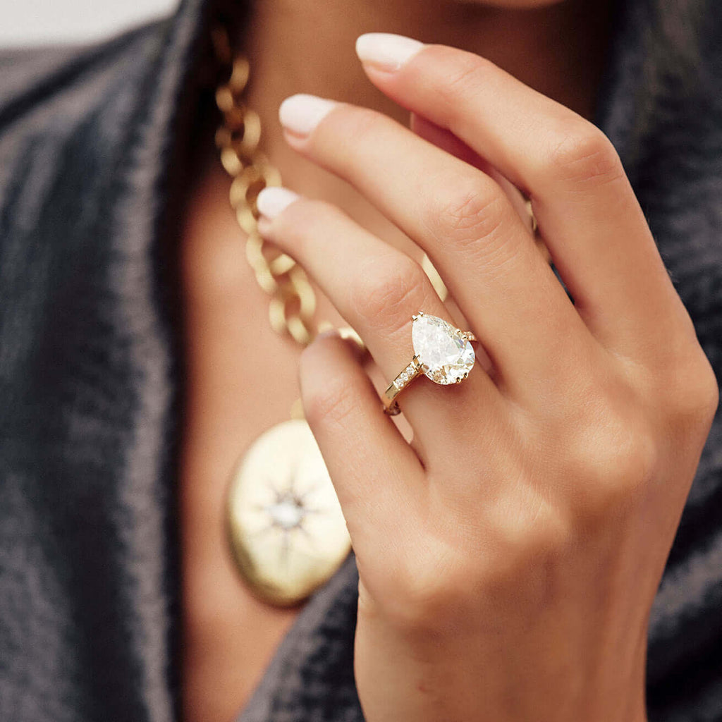 Woman's hand wearing an engagement ring featuring an antique pear shape diamond.