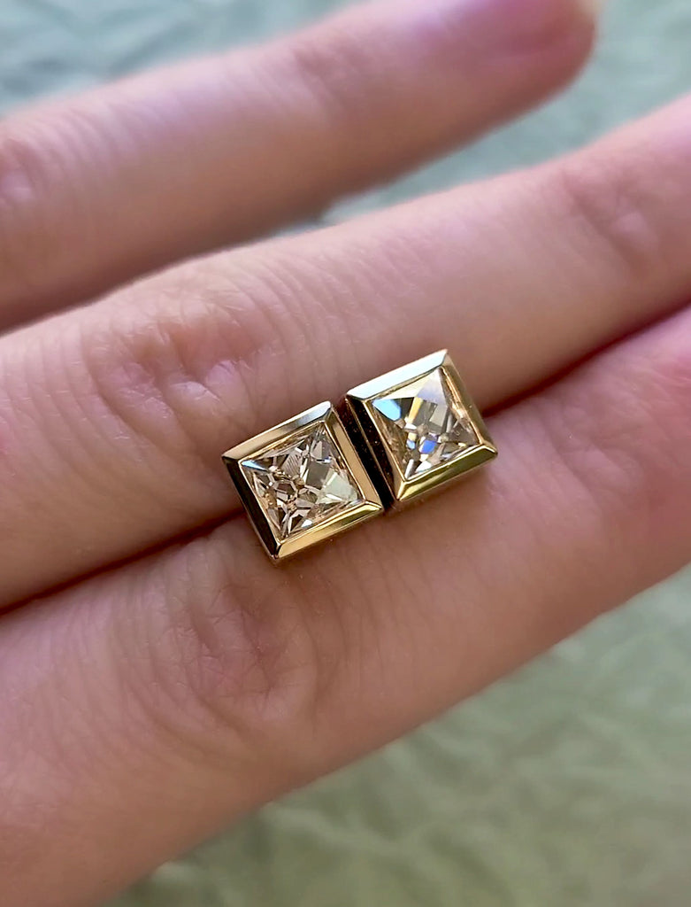 French cut diamonds bezzle set in yellow gold stud earrings, held out in a person's hand