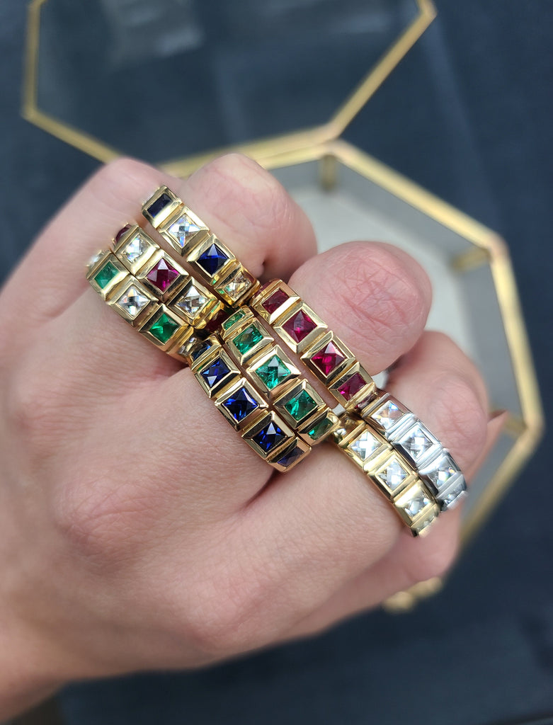 Single Stone's 'Karina' eternity bands featuring French cut diamonds, rubies, emeralds, and sapphires in yellow gold and platinum settings stacked on a woman's fingers