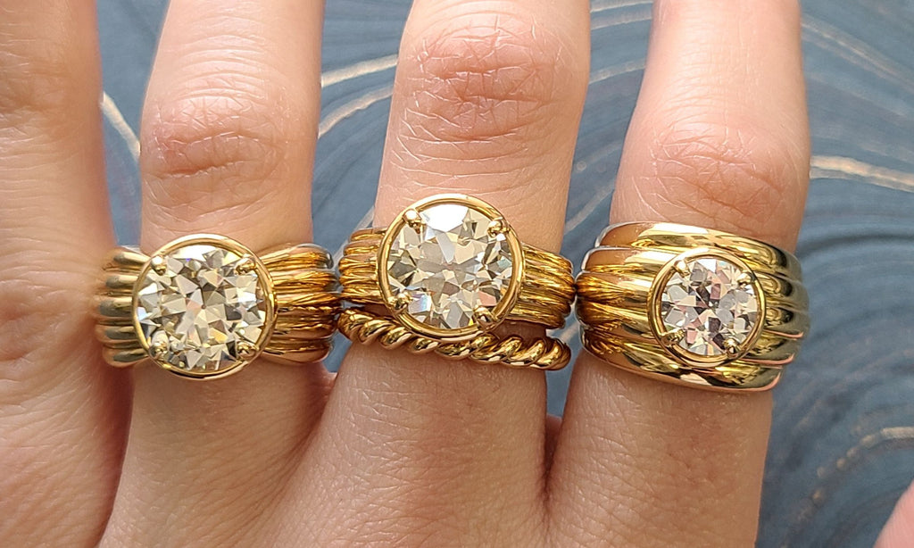 Three bold gold 'Eleni' rings featuring old European cut diamonds on a woman's hand, each on a different finger, with a twisted gold band stacked below the middle ring