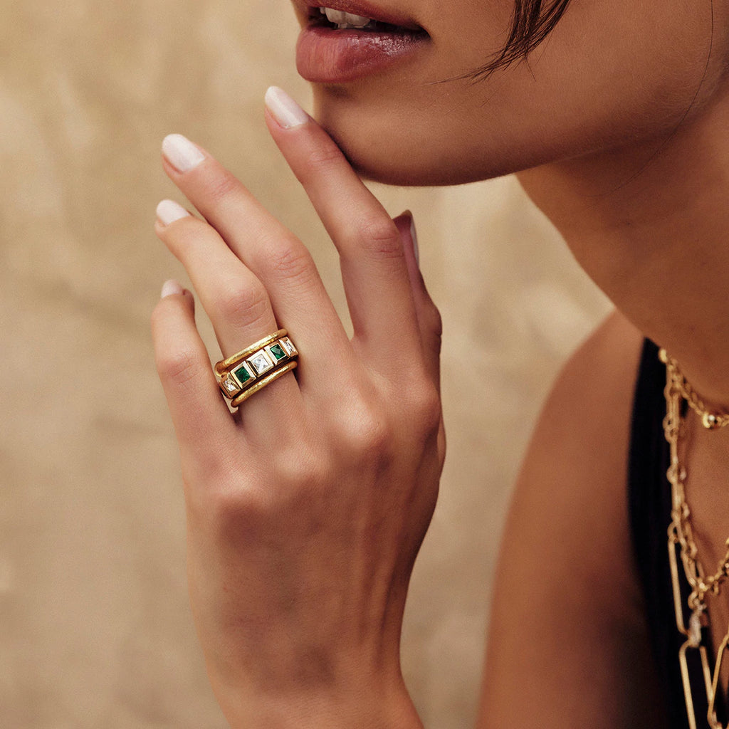 Woman's hand touching her face wearing a Single Stone eternity band featuring French cut emeralds and diamonds