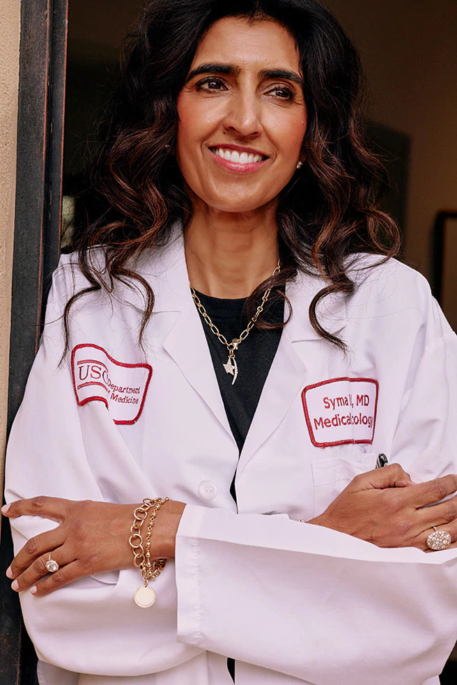 Single Stone client Syma wearing her white doctor's coat and a variety of pieces from Single Stone's fine jewelry collection