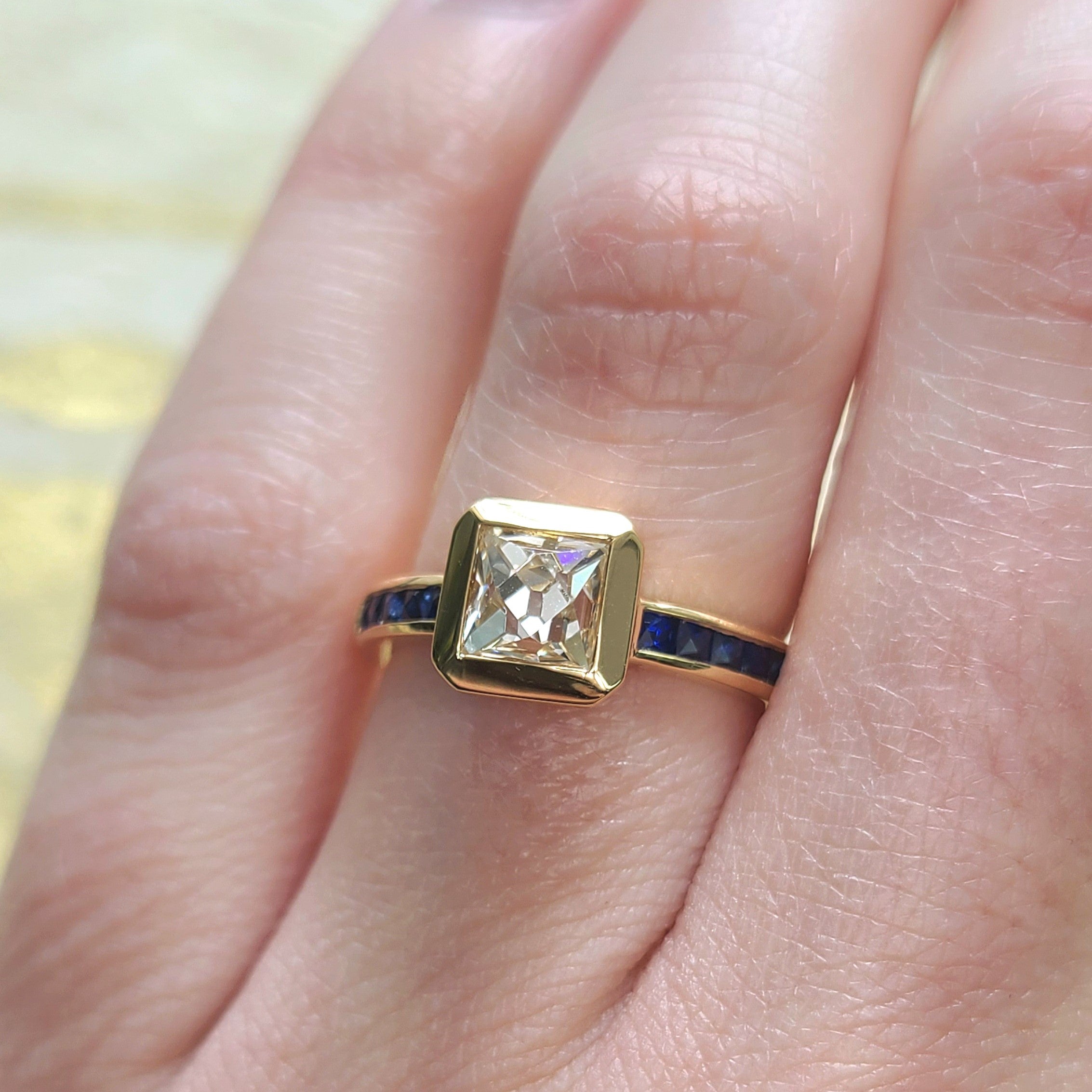 SINGLE STONE KARINA RING featuring 1.15ct K/VS1 GIA certified French cut diamond with 0.39ctw French cut blue sapphire accent stones bezel set in a handcrafted 18K yellow gold mounting.